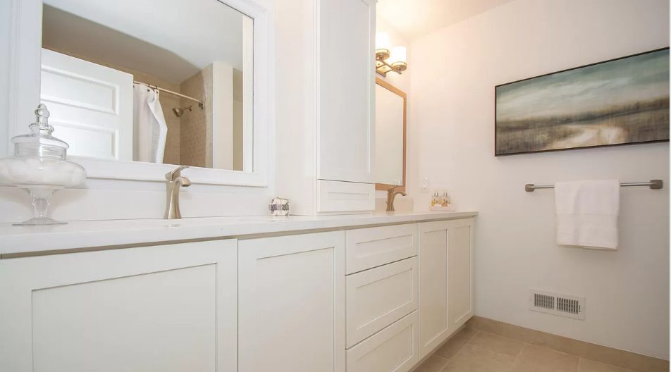 Primary bathroom with white double vanity, framed mirrors and landscape artwork