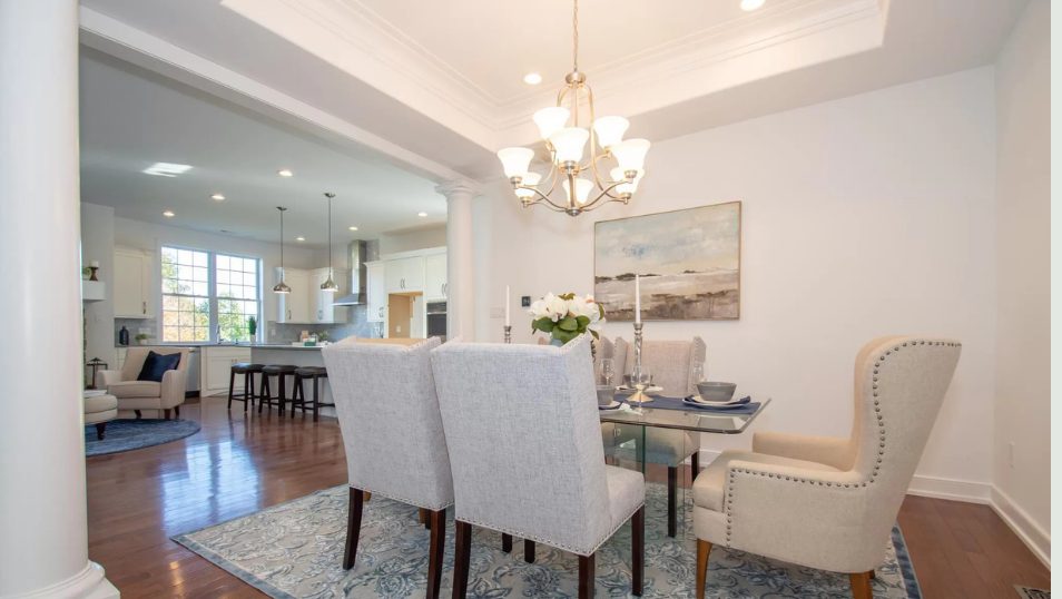Dining room with chandelier, upholstered chairs, columns and open kitchen beyond